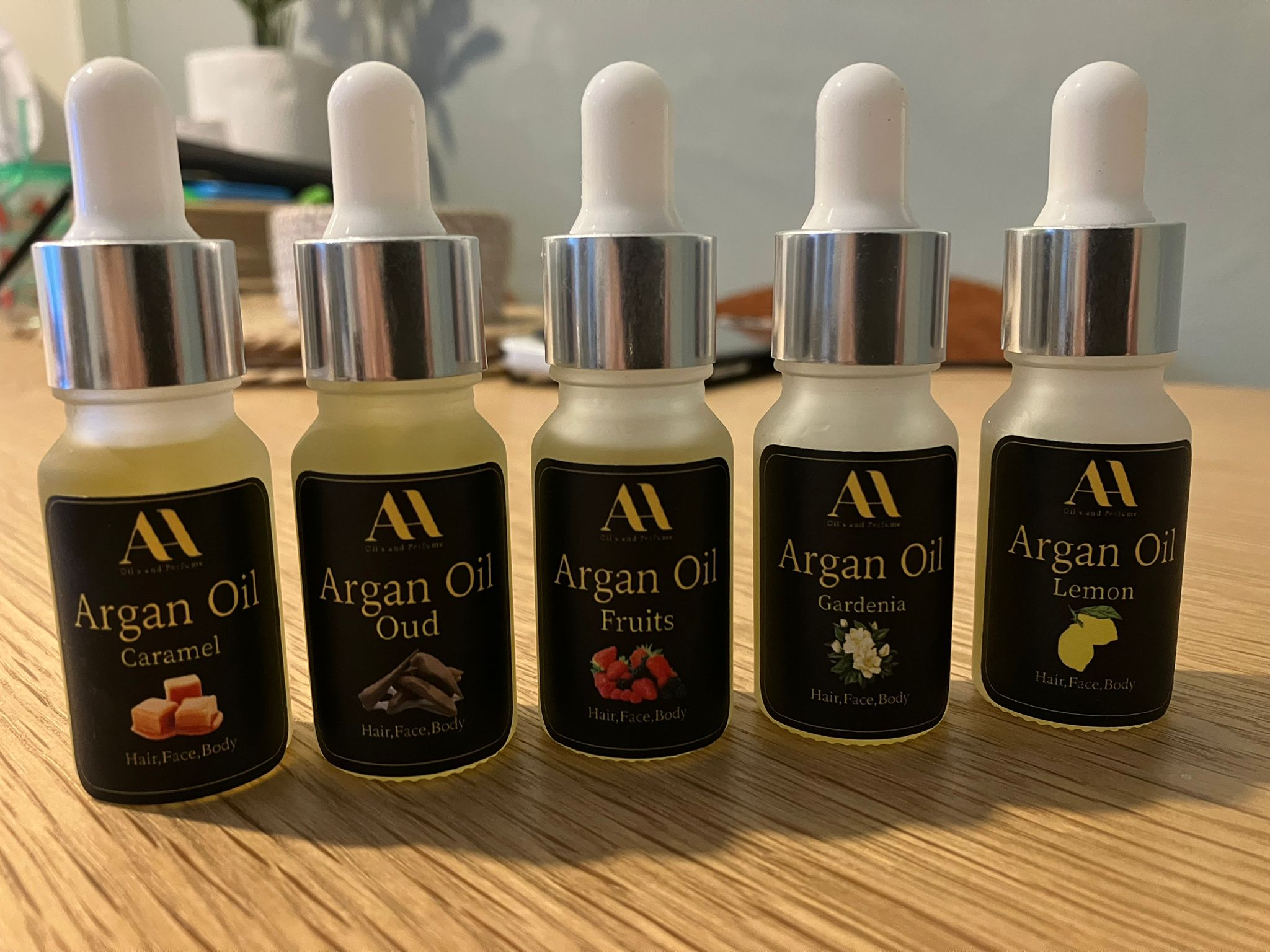 Five bottles of argan oil with different scents on a wooden surface.